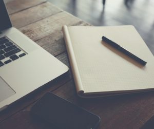 Picture of notepad and pen on a desk next to a laptop