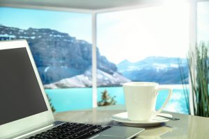 laptop on desk with view of lake and mountains