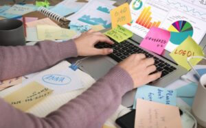 Guest Blog: Overcoming Overwhelm: Discovering More Ease at Work - picture of hands at a keyboard covered in post it notes